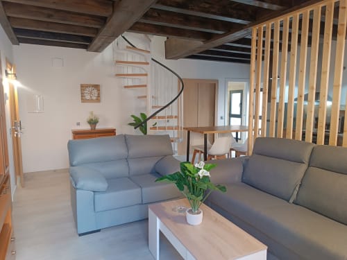 Sala moderna de apartamento en Ávila con asientos cómodos, escalera de caracol, vigas de madera y plantas en macetas