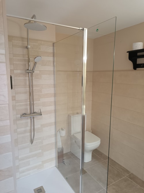 Baño moderno con cabina de ducha de cristal, dos duchas tipo lluvia, inodoro blanco y paredes con azulejos beige en Apartamentos