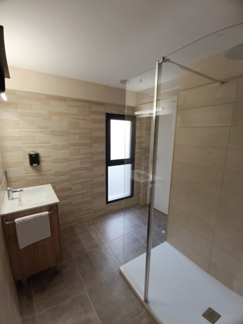 Baño moderno en Apartamentos Turísticos Ávila con ducha a ristras, lavamanos y piso en azulejos beige