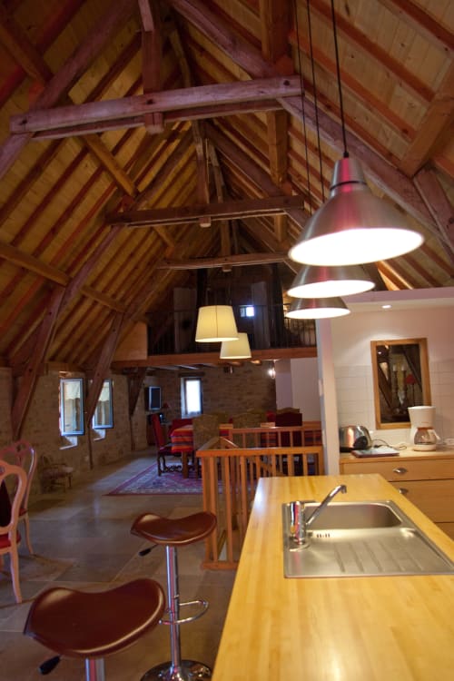 Intérieur de gîte ouvert avec poutres en bois apparentes, comptoir de cuisine, bar et salle à manger aux Chambres d'hôtes Les