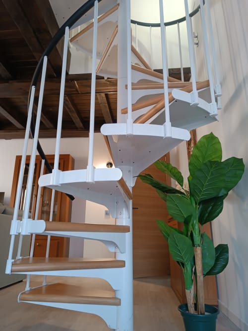 Escalera de caracol moderna con marco blanco y peldaños de madera en apartamento de Ávila, diseño accesible con decoración de plantas verdes.