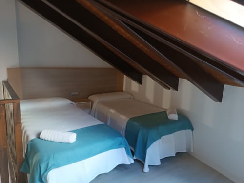 Acogedora habitación en buhardilla de Apartamentos Turísticos Ávila con dos camas individuales, mantas azules y vigas de madera inclinadas