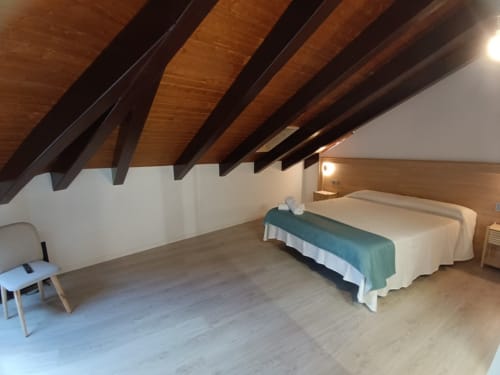 Amplio dormitorio en buhardilla de Apartamentos Turísticos Ávila con vigas de madera, camas gemelas, pisos de parqué y vistas a la ciudad