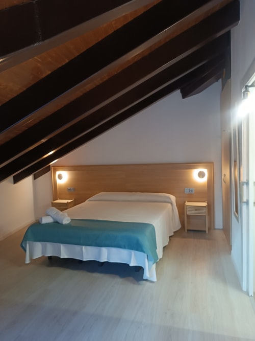 Dormitorio moderno en Apartamentos Turísticos Ávila con techo de vigas, cabecero de madera, ropa de cama color azul verdoso y diseño contemporáneo