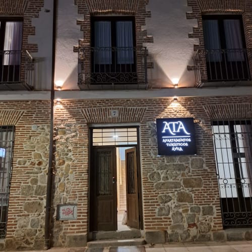 Entrada nocturna de Apartamentos Turísticos Ávila, fachada de ladrillo con rótulo iluminado, ubicado en Ávila, España