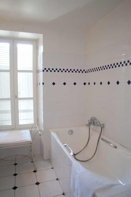 Salle de bains lumineuse avec baignoire blanche, frise carrelage bleu et équipements classiques aux Chambres d'hôtes Les Pratges à Figeac