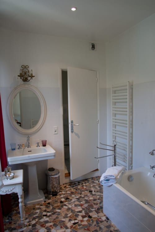 Salle de bains élégante de la Chambre Lisa aux Pratges, Figeac, avec lavabo sur colonne, miroir ovale, baignoire et radiateur-sèche-serviettes