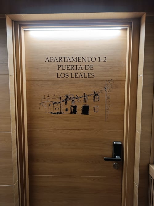 Puerta de madera de entrada al Apartamento 1-2 en Puerta de Los Leales, Ávila, con grabado arquitectónico del edificio