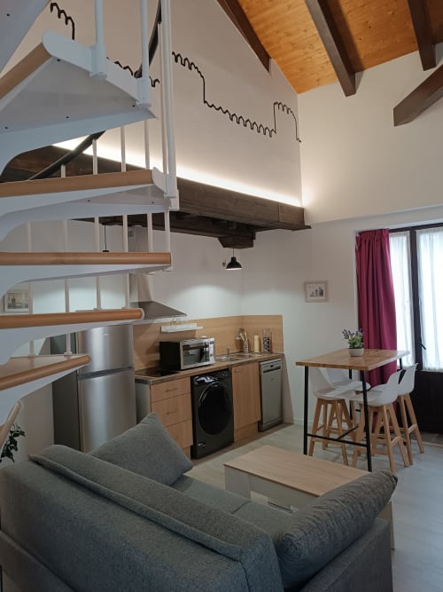 Moderno apartamento estudio en Ávila con cocina abierta, escalera de caracol, comedor y sofá gris bajo techos abovedados.