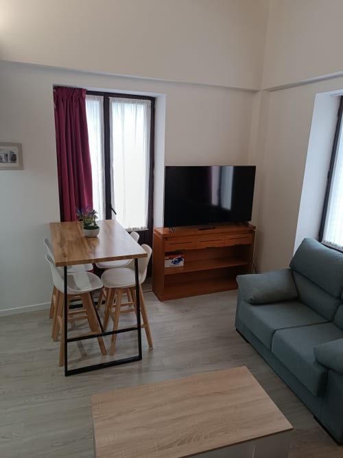 Sala de estar moderna en Ávila con mesa de comedor, sofá gris, mueble de TV en madera y vistas a la ciudad desde puertas de cristal