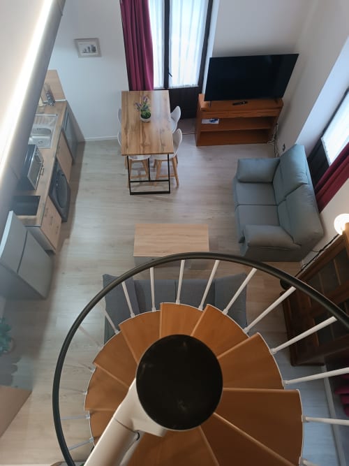 Vista en espiral de moderno apartamento en Ávila con mesa de comedor, sofá gris y TV en sala abierta