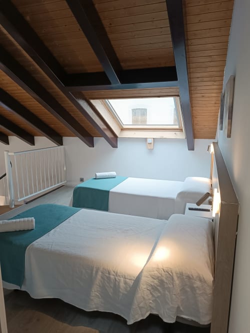 Luminoso dormitorio abuhardillado en Apartamentos Turísticos Ávila con dos camas, vigas de madera, claraboya y vistas a la ciudad