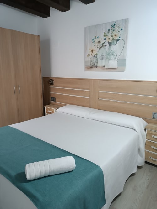 Dormitorio moderno en Apartamentos Turísticos Ávila con muebles de madera, ropa de cama blanca y arte floral en las paredes