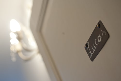 Plaque noire « Lucovi » sur mur blanc dans la Chambre Lucas à la maison d'hôtes Les Pratges, Figeac