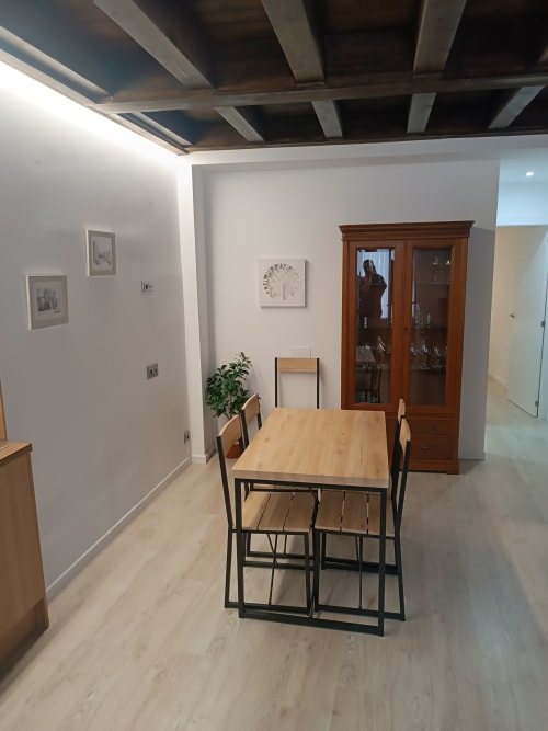 Comedor moderno en apartamento de Ávila con mesa de madera, sillas negras, vitrina de cristal y paredes blancas