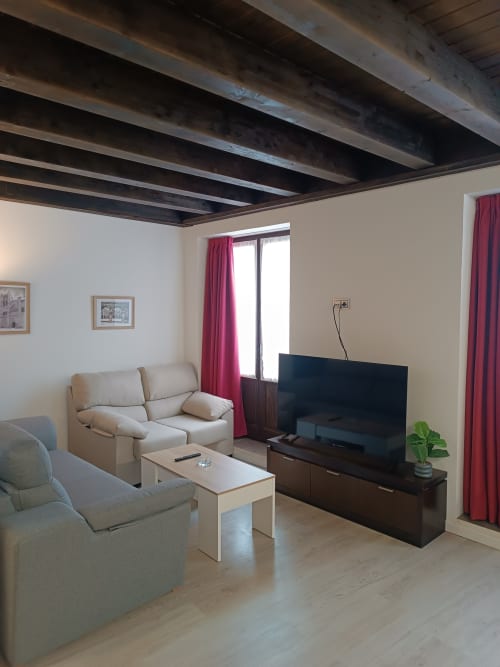 Sala de estar moderna en Ávila con sofá beige, televisor de pantalla plana, vigas de madera oscura y cortinas rojas