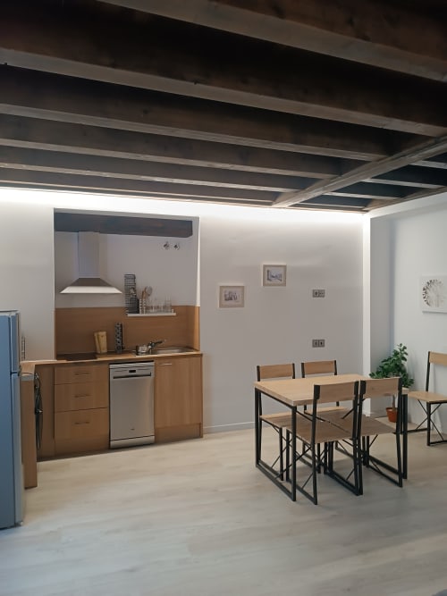 Moderna cocina-comedor en apartamento de Ávila con muebles de madera, electrodomésticos de acero inoxidable y mesa para cuatro.