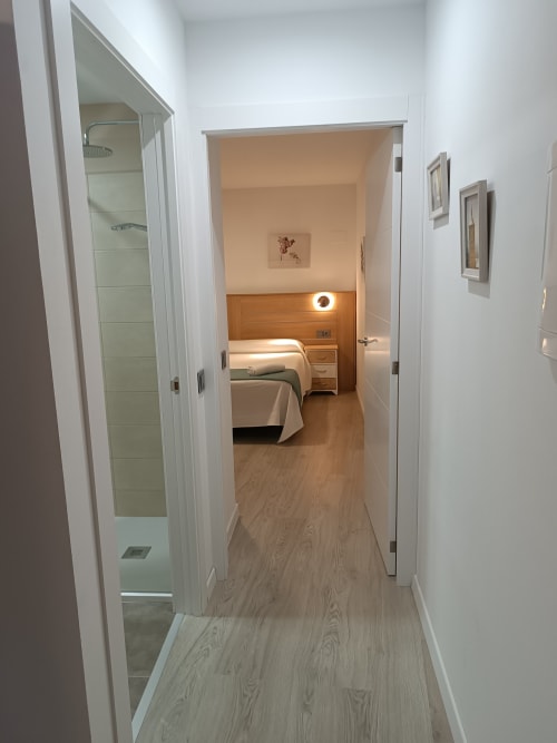 Vista del pasillo del departamento en el hotel Ávila con dormitorio, baño y pisos de madera