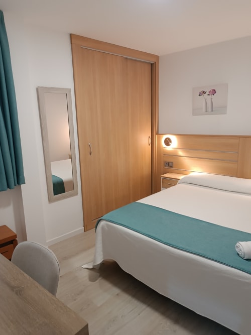 Moderno dormitorio de hotel en Apartamentos Turísticos Ávila con cama de madera, sábanas blancas y manta decorativa en azul verdoso