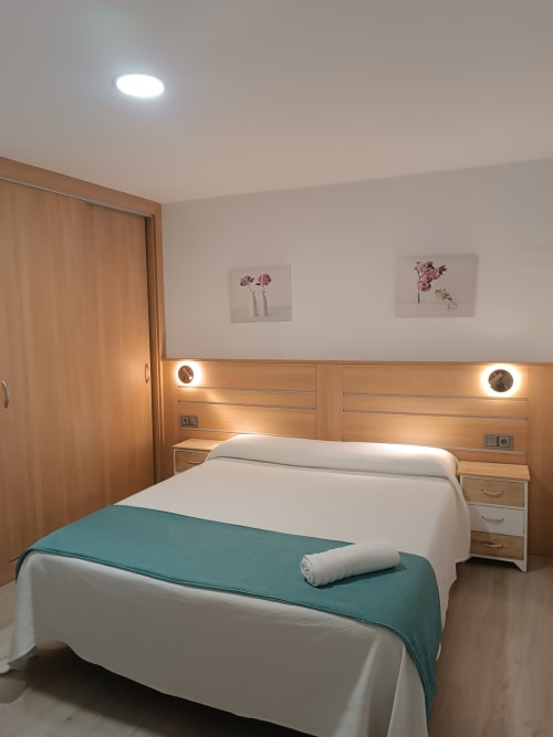 Dormitorio moderno en Apartamentos Turísticos Ávila con cabecero de madera, ropa de cama blanca, manta turquesa y arte floral en la pared
