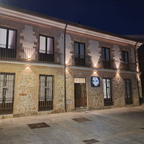 Apartamentos Turísticos Ávila fachada de piedra histórica al anochecer, detalles de ladrillo, balcones de hierro forjado