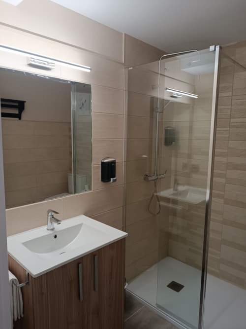 Baño moderno con lavamanos blanco, mueble de madera, espejo grande y ducha a ras de suelo en Apartamentos Turísticos Ávila, España