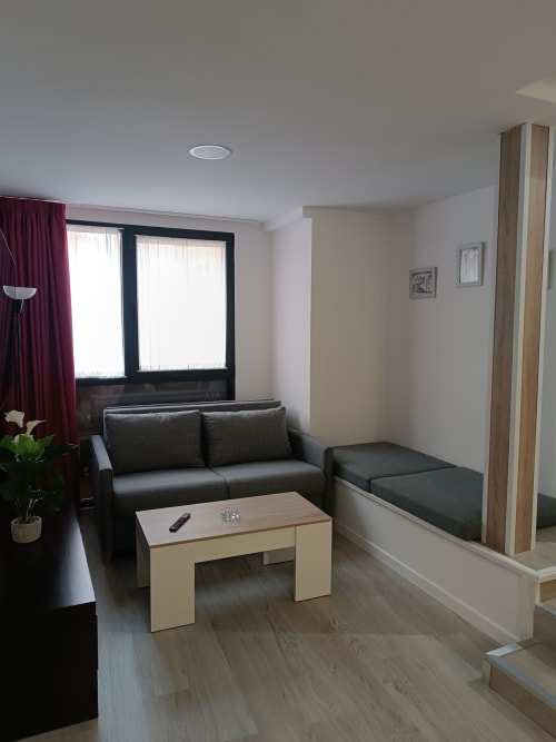 Elegante sala de estar en Apartamentos Turísticos Ávila con sofá gris, mesa de madera clara, amplios ventanales y detalles en burdeos