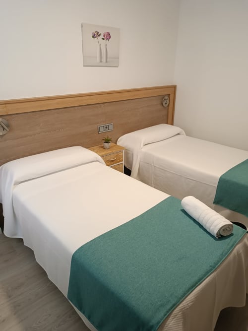 Dos camas individuales con sábanas blancas y cobertores verdes en habitación del hotel Apartamentos Turísticos Ávila