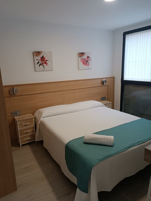Habitación moderna en Apartamentos Turísticos Ávila con cabecero de madera, ropa de cama blanca, banco turquesa y arte floral en la pared