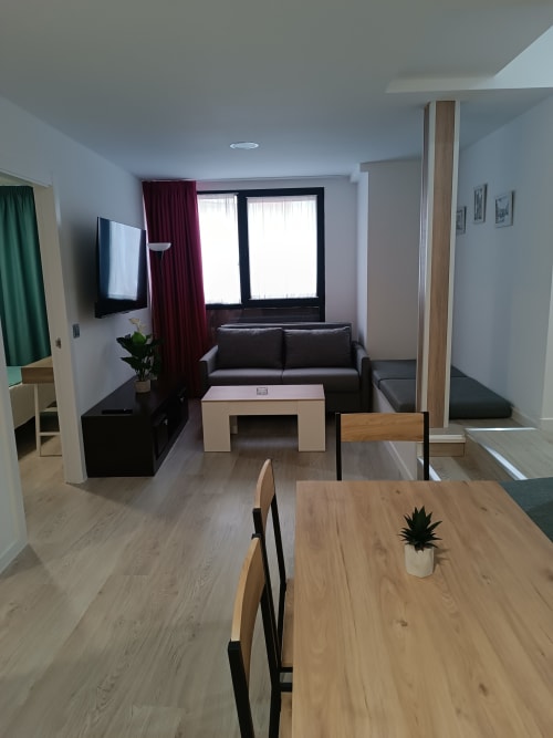 Moderno salón de apartamento en Ávila con mesa de comedor, sofá negro, televisor y vistas a la ciudad
