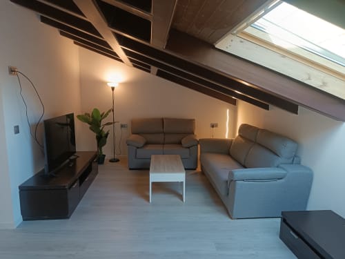 Sala de estar moderna en ático de apartamento en Ávila con sofás grises, televisión, claraboya y mobiliario contemporáneo
