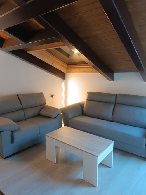 Sala moderna en apartamento de Ávila con sofás grises, mesa blanca, vigas de madera y luz natural