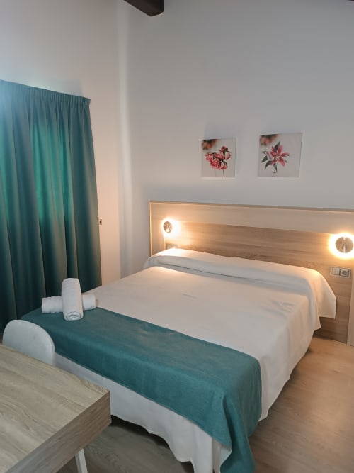 Moderno dormitorio de hotel en Apartamentos Turísticos Ávila con cama queen, detalles en verde azulado y vista a la ciudad de Ávila, España