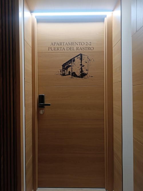 Entrada con puerta de madera al Apartamento 2-2 Puerta del Rastro en Apartamentos Turísticos Ávila con obra de arte de edificio en ruinas