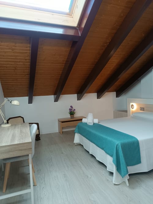 Moderna habitación en desván del hotel Ávila con vigas de madera vista, cama, escritorio y flores púrpura