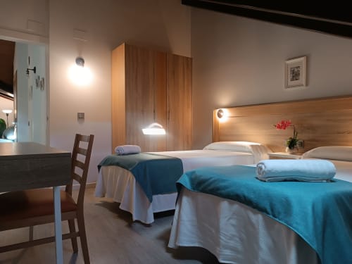 Moderno dormitorio doble en Apartamentos Turísticos Ávila con mantas azules, cabecero de madera y zona de comedor