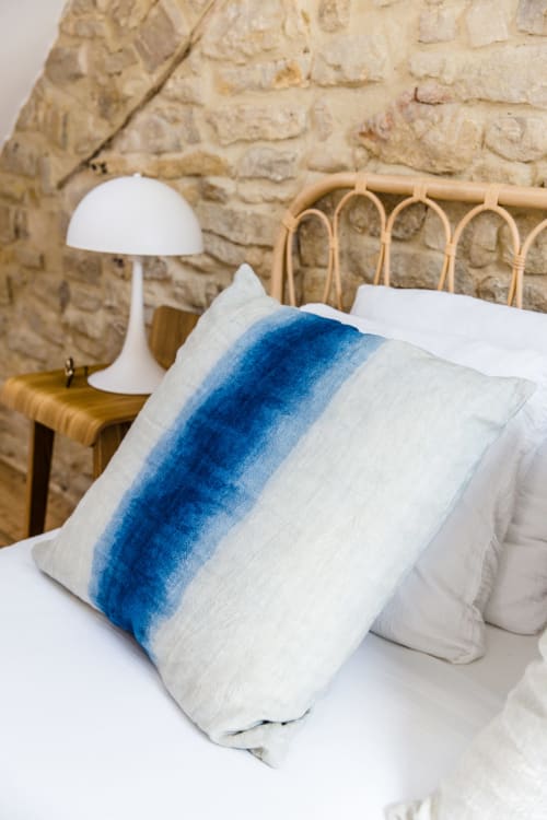 Chambre côtière aux Filles du Bord de Mer avec oreiller à rayures bleues, literie blanche, tête de lit en rotin et mur en pierre