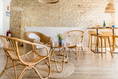 Salon côtier lumineux avec fauteuils en osier, murs en pierre et touches de bois aux Filles du Bord de Mer,