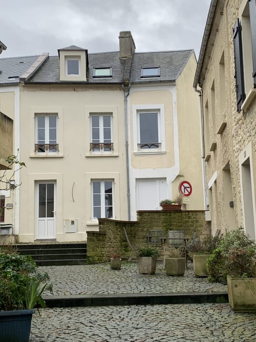 Cream-colored cottage at Les Filles du Bord de Mer, Port-en-Bessin, with slate roof and sea-view windows