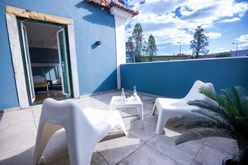 Terraço moderno no telhado do VAGO Alcântara Suites, Lisboa, com espreguiçadeiras brancas, paredes azuis e vistas da cidade