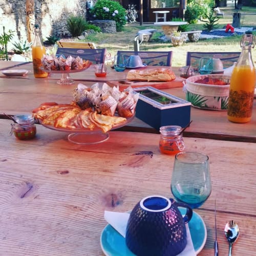 Table de petit-déjeuner à la Bastide du Thoré avec viennoiseries, jus frais et vaisselle bleue, vue sur Labastide-Rouairoux
