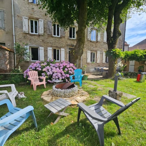Parc accueillante de la Bastide du Thoré avec ses chaises Adirondack colorées, hortensias violets et foyer à Labastide-Rouairoux