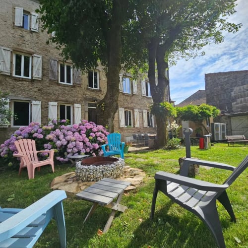 Cour en pierre de la Bastide du Thoré avec hortensias roses, chaises Adirondack et foyer à Labastide-Rouairoux