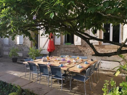 Espace de déjeuner en plein air à la cour de Bastide du Thoré à Labastide-Rouairoux avec table en bois, chaises bleues et végétation luxuriante