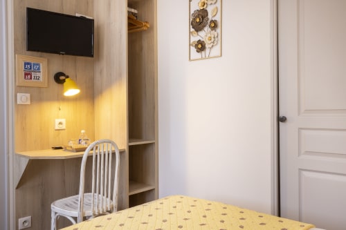 Chambre simple standard de l'Hôtel De Lion Sur Mer avec bureau jaune, télévision, fauteuil et décoration murale florale à Lion sur Mer