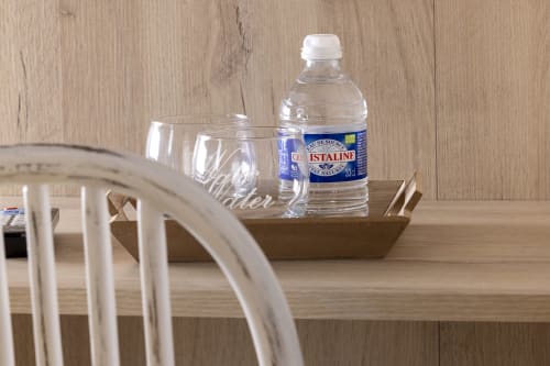 Plateau de services en chambre Hotel De Lion Sur Mer avec bouteille d'eau Cristaline et verres sur bureau en bois