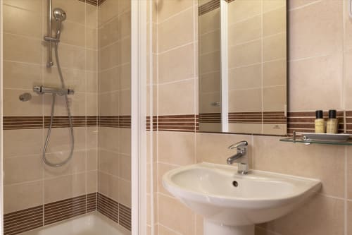 Salle de bains moderne de la chambre standard Hôtel De Lion Sur Mer avec carrelage beige, douche, lavabo et rangements