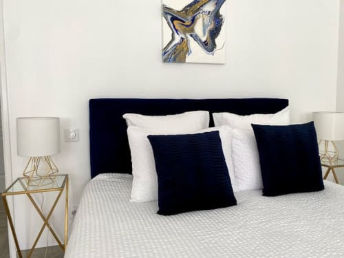 Modernes Schlafzimmer im Domaine de Bize mit marineblanem Kopfteil, weißen Kissen, dunklen Dekokissen, goldenen Nachttischen und abstrakten Wanddekoren