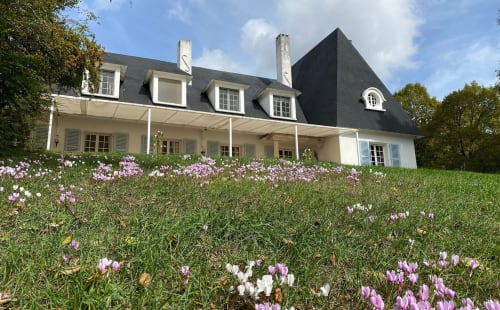 Elegant French manor house with mansard roof, white shutters, and blooming wildflowers in Mirepoix, Ariège