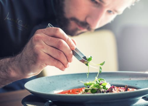 Chef presentando microverdes sobre un plato de salsa roja en Domaine de Bize, Mirepoix